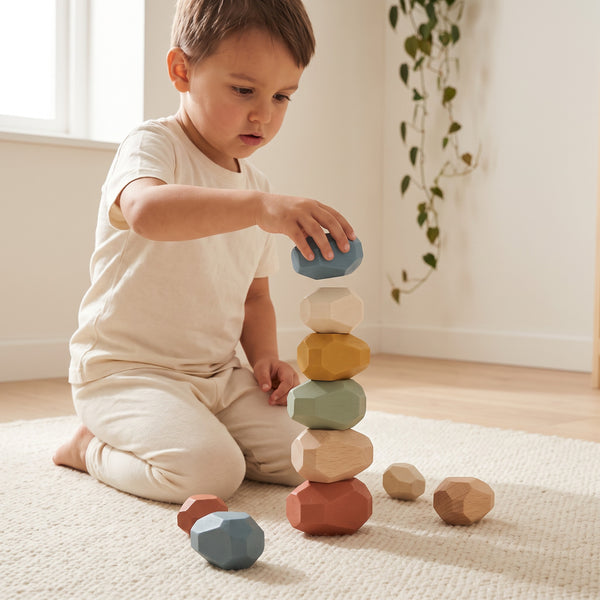 Child carefully balancing one more stone on a wobbling tower of wooden pebbles