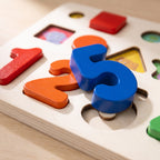 Macro of chunky painted wooden numerals seated in their cut-outs on the birch matching board
