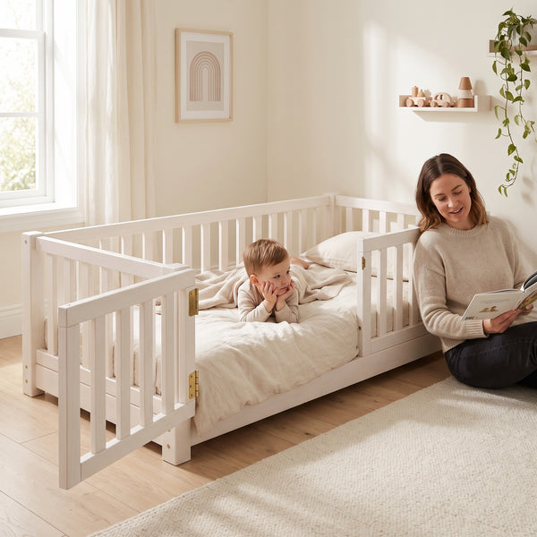 Parent sitting beside the twin size white Montessori floor bed reading to their toddler