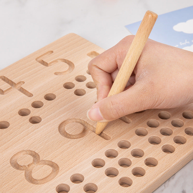 Child's hand using a wooden stylus to trace the engraved numeral 5 groove on the birch number board, with rows of counting holes below