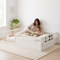 Parent stretched out inside the full size white Montessori floor bed reading a picture book with their toddler