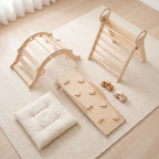 All pieces of the natural wood Pikler triangle set laid out: triangle, rocking arch, ramp, two wooden cars and cushion