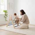 Parent kneeling beside the blue Pikler triangle spotting their toddler as they climb