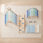 All pieces of the blue Pikler triangle set laid out: triangle, rocking arch, ramp, two wooden cars and cushion