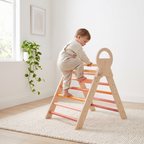 Toddler climbing the rungs of the orange wooden Pikler triangle