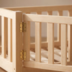 Close-up of the brass barrel hinges on the gate of the oak Montessori floor bed, showing the pine grain and joinery
